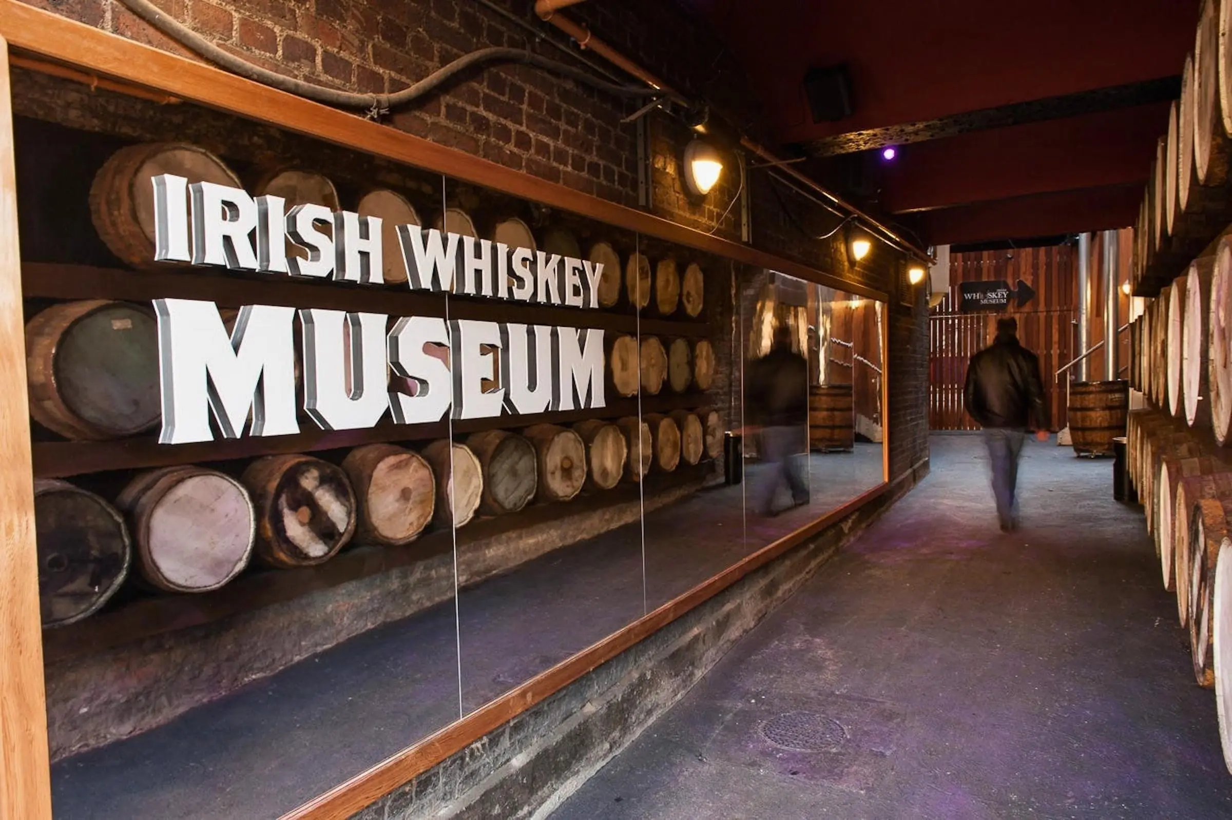 Irish Whiskey Museum Entrance Large Irish Whiskey Museum sign over a glass display of wooden whiskey barrels in a brick corridor