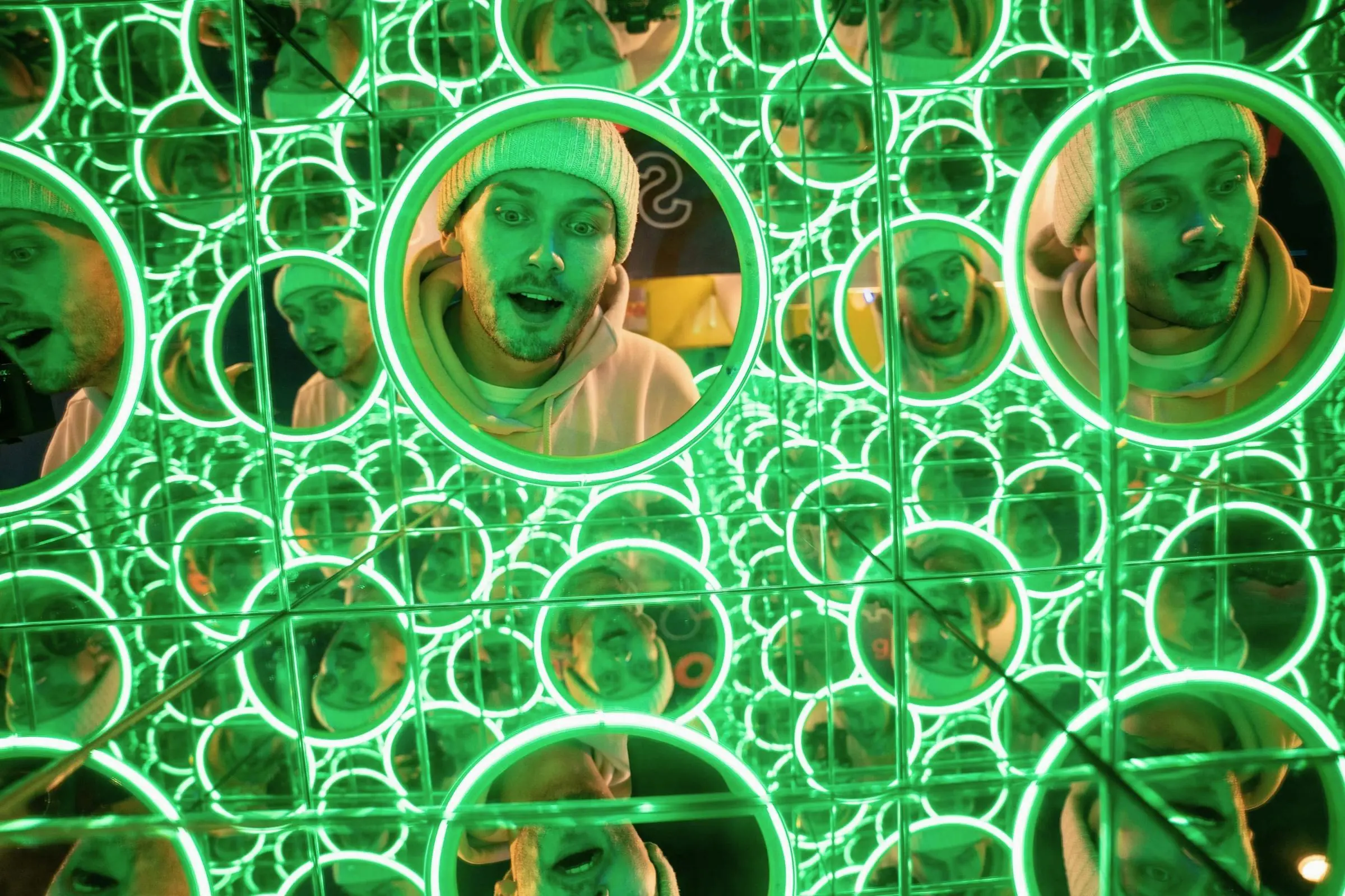 Multiple reflections of a visitor in a green neon mirror maze at World of Illusion Dublin